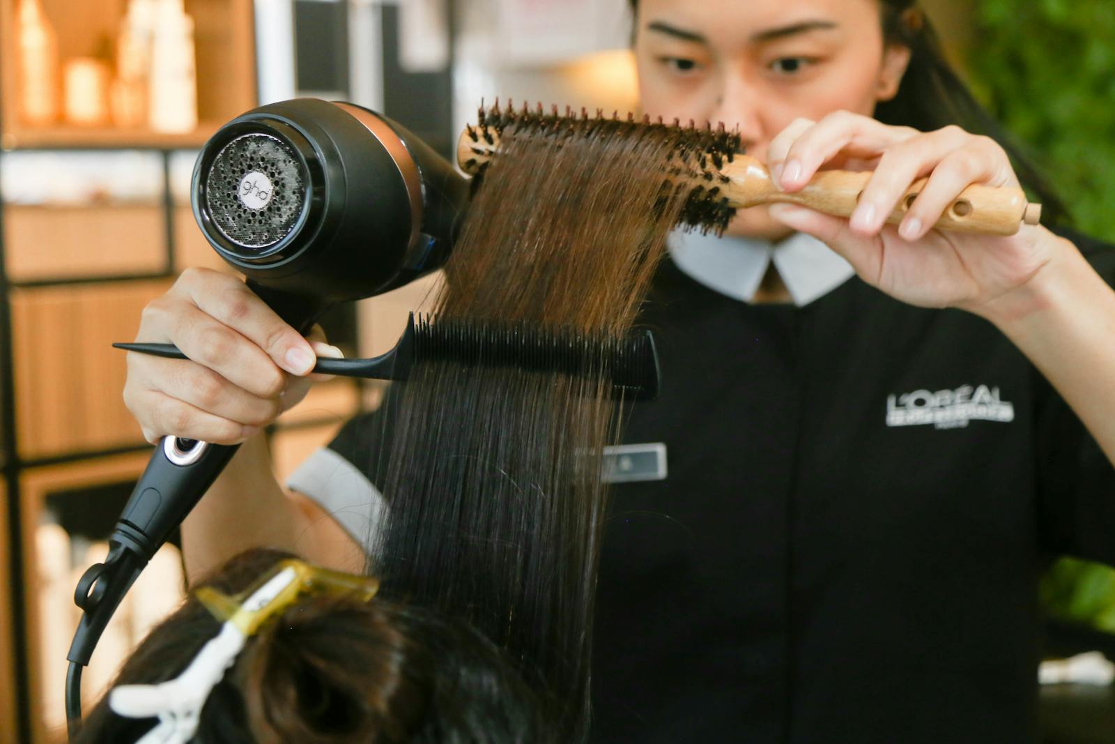 Hairdresser expertly styles hair using a brush and dryer in a salon setting.