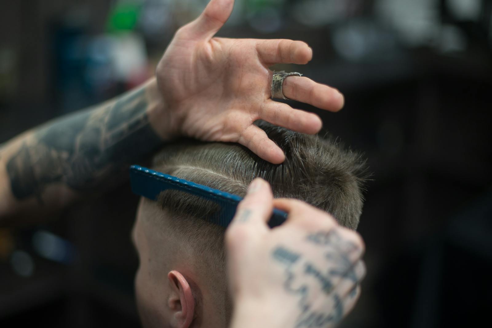 Close-up of a tattooed barber giving a stylish haircut indoors, highlighting modern grooming techniques.