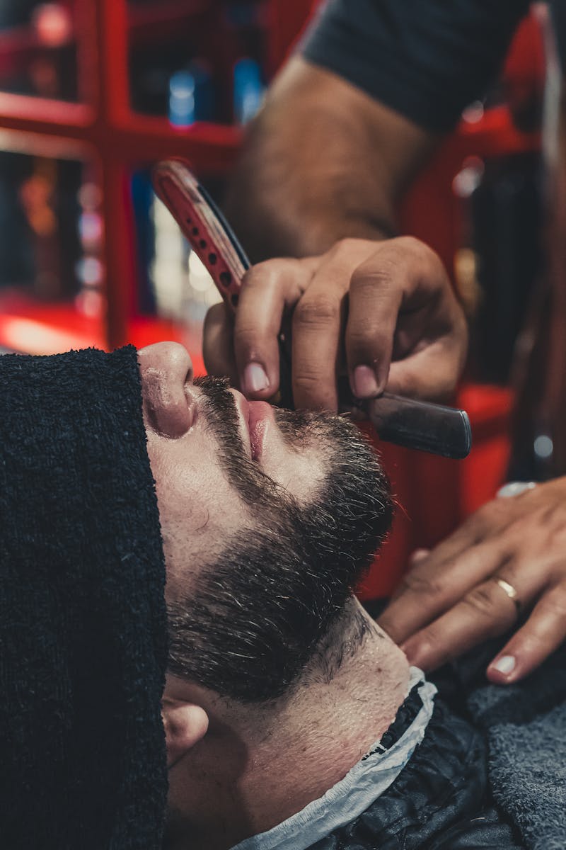 A barber skillfully shaves a man's beard using a straight razor at a barbershop.