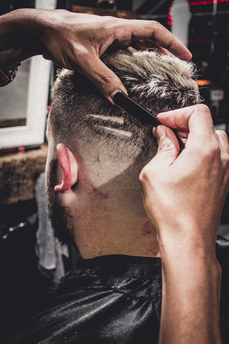 A man receives a detailed haircut with a straight razor at a barbershop, showcasing modern style.