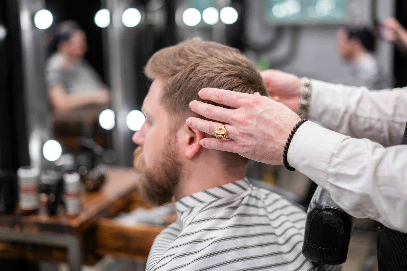 Barber styling a bearded man's hair in a modern barbershop setting.