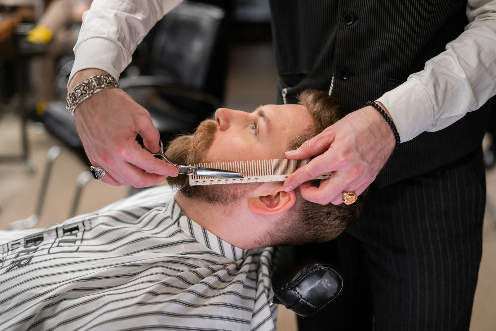 A skilled barber meticulously trims a client's beard using comb and scissors in a modern barbershop.