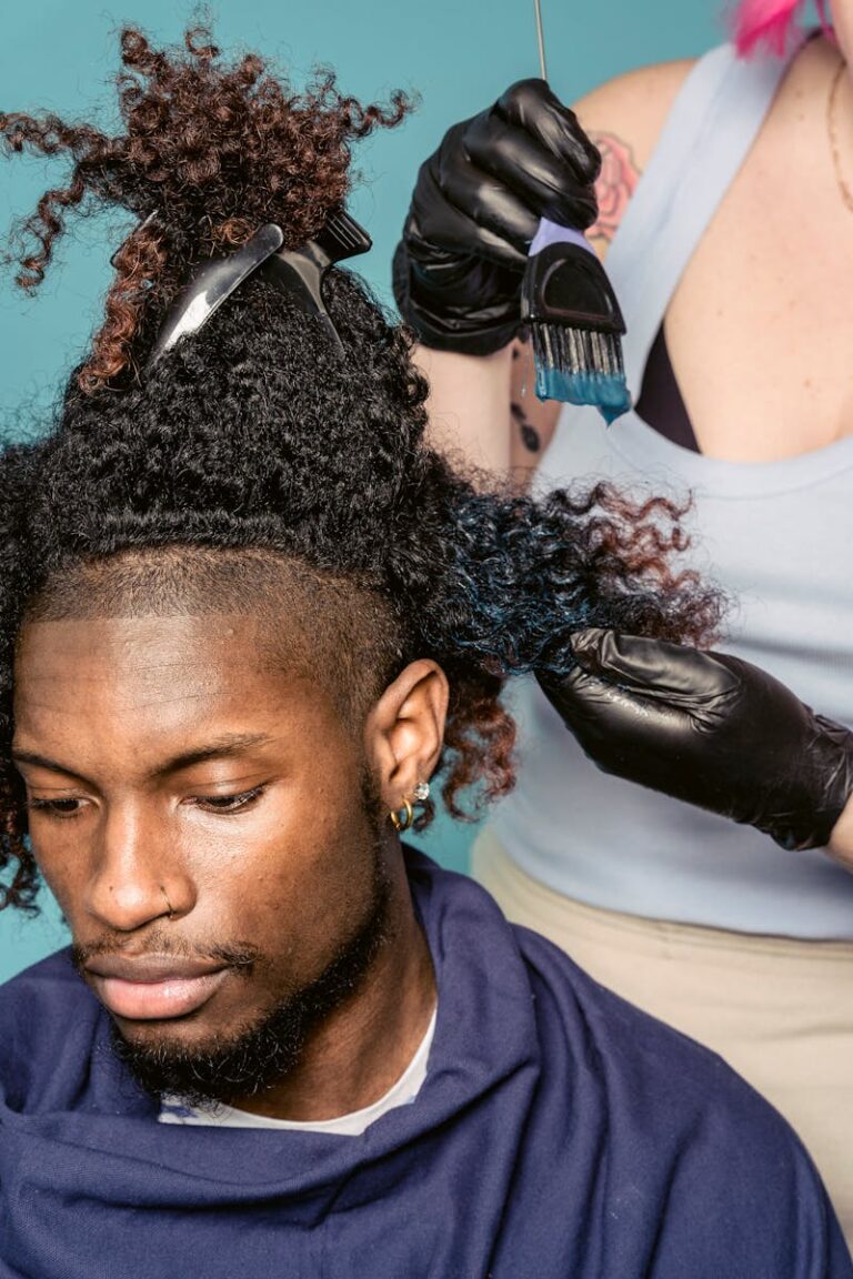 A hairstylist wearing gloves applies blue dye to a man's curly hair in a salon.