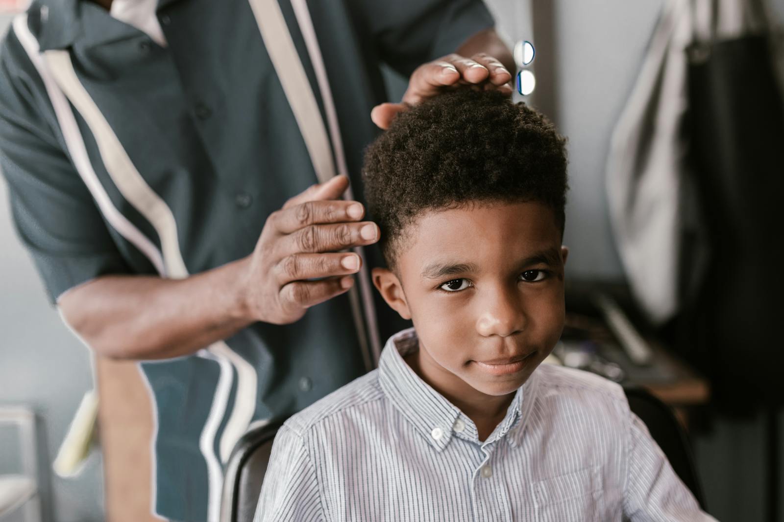 Adorable boy with curly hair enjoys a haircut at a barber shop.