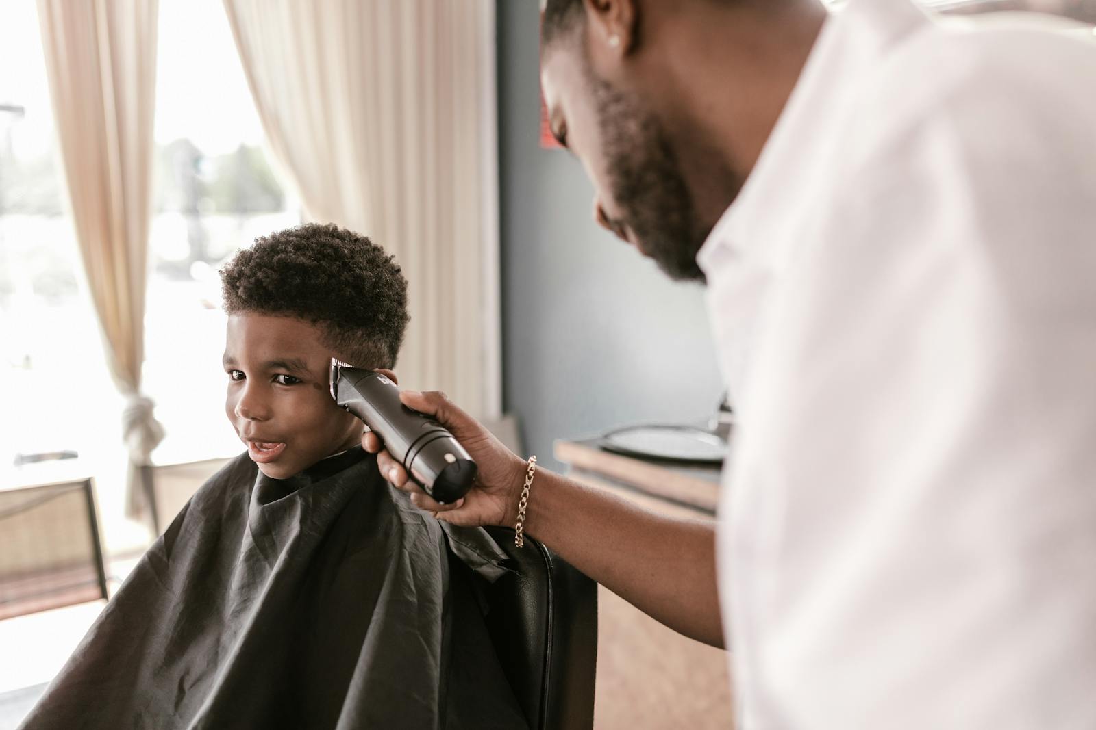 A young boy receives a haircut from a barber using electric clippers inside a barbershop.