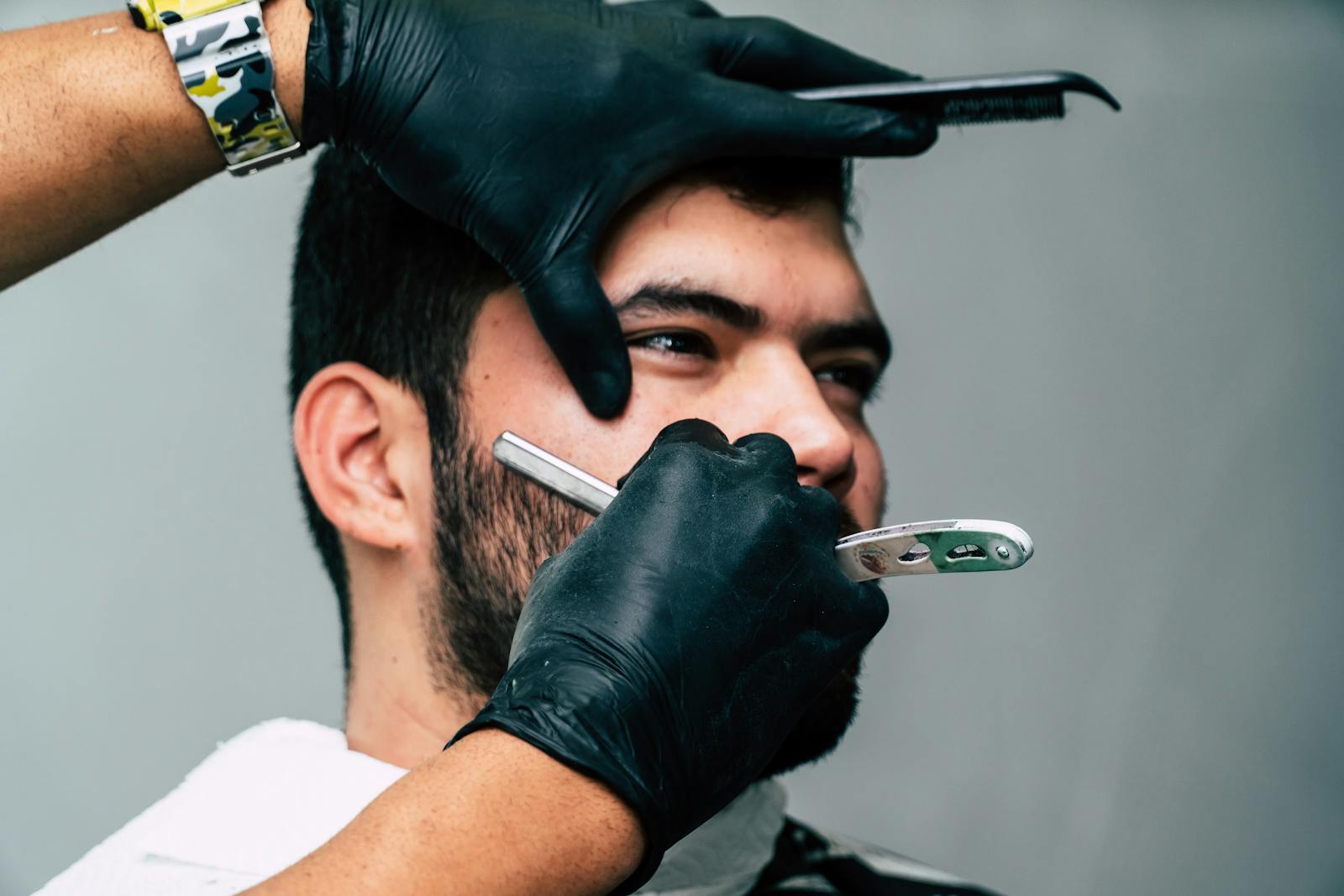 Close-up of a barber shaving a man's beard with precision in a contemporary barbershop setting.