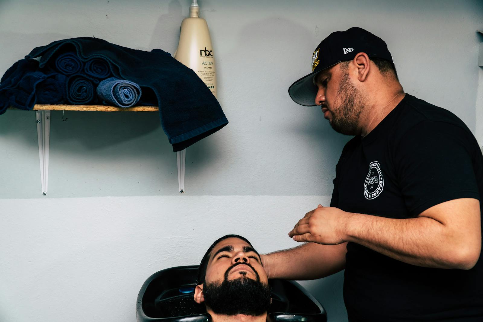 A barber grooming a client's beard in a modern barbershop setting.