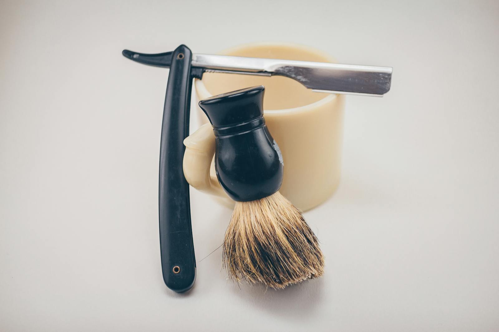 Still life of barber tools including a straight razor, shaving brush, and mug.